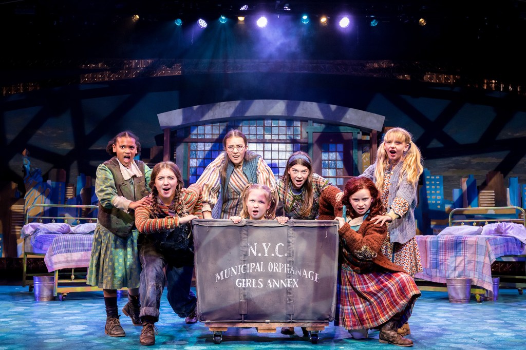Seven girls playing the orphans in a production of "Annie" at Chanhassen Dinner Theaters standing across a stage with one in a laundry cart